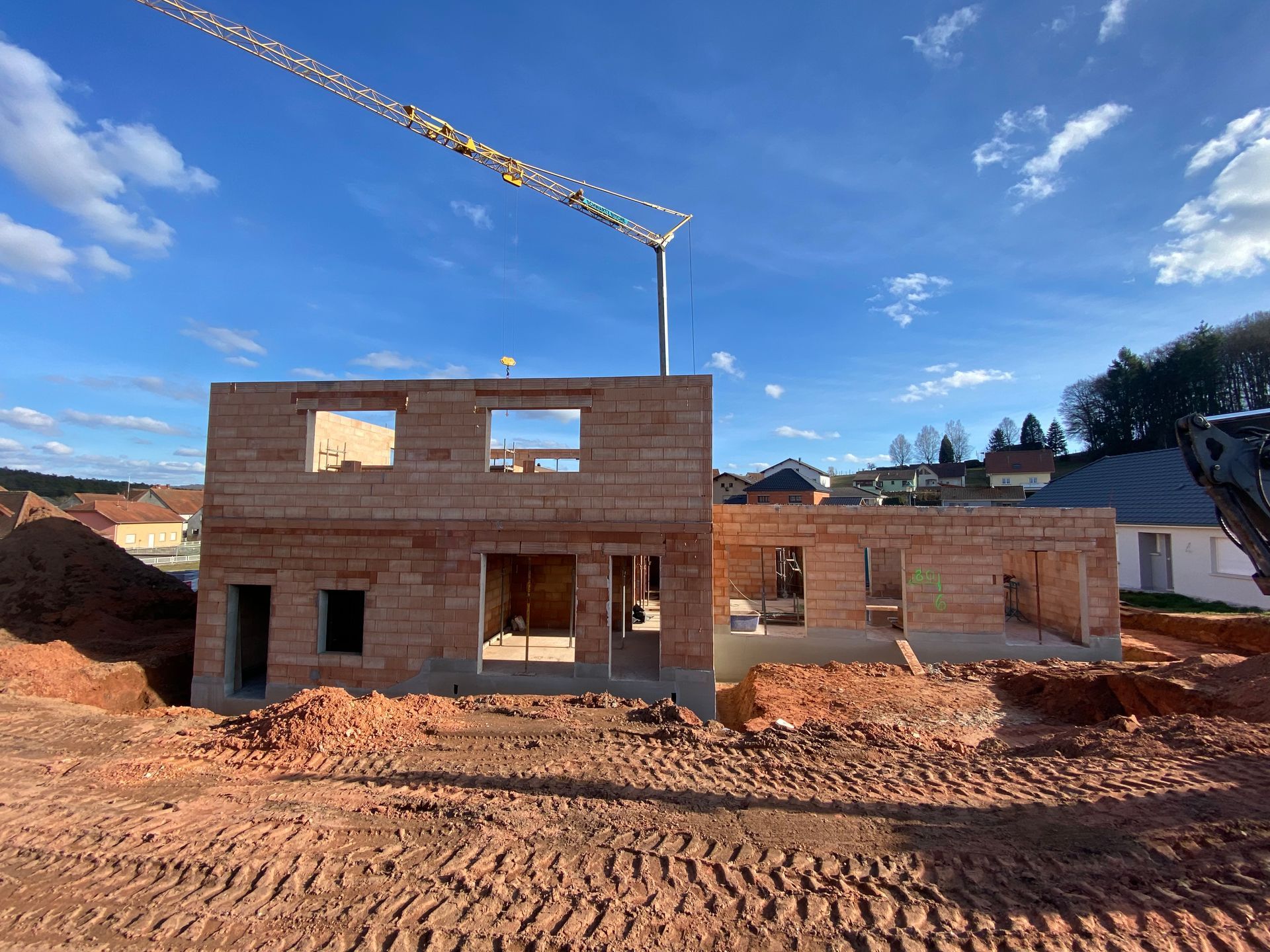 Maison en briques partiellement construite, en cours de construction, avec une grue se détachant sur un ciel bleu clair.