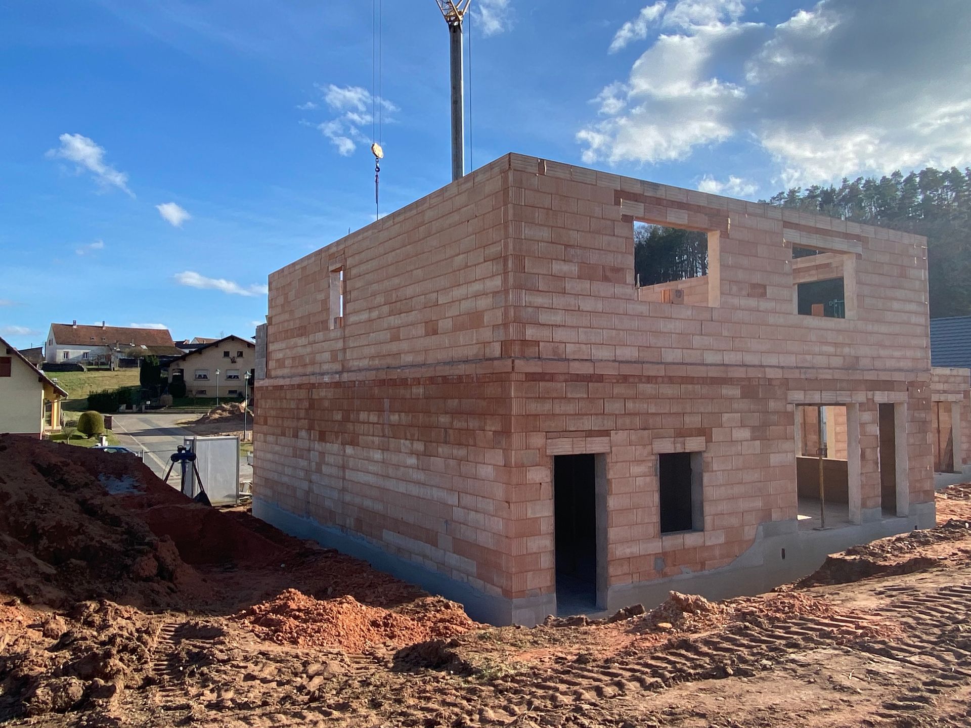 Maison en briques de deux étages partiellement construite sur un terrain en terre battue sous un ciel bleu