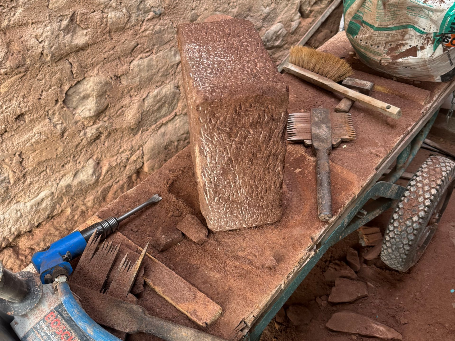 Outils de construction et briques sur une charrette poussiéreuse à côté d'un mur de pierre.