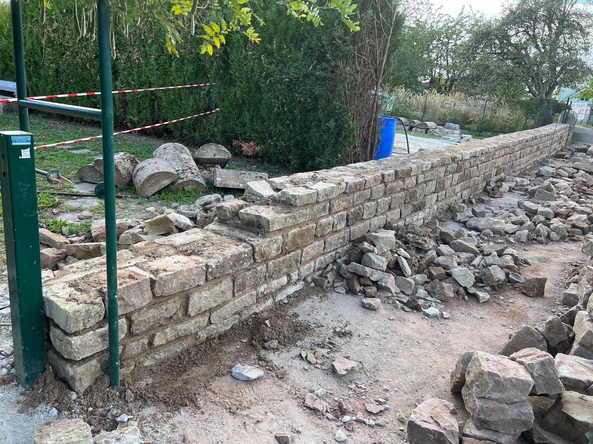 Mur de soutènement en pierre en construction à côté d'un chemin de gravier et d'un portail vert à l'extérieur