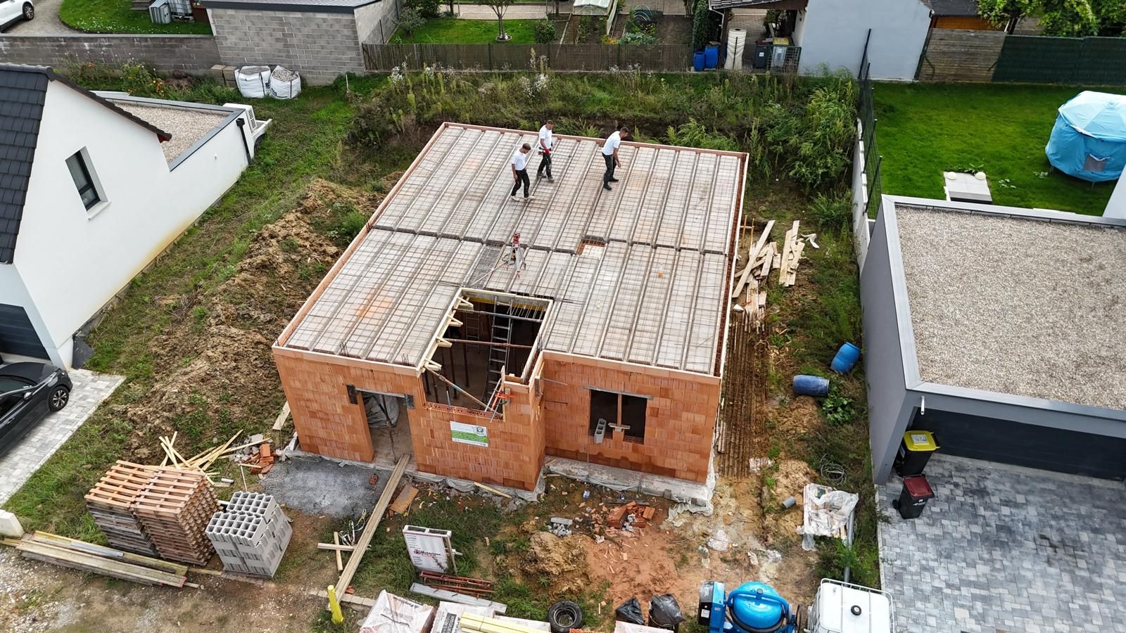Vue aérienne par drone d'une maison en briques en construction, avec des couvreurs et une grande ouverture dans le toit.