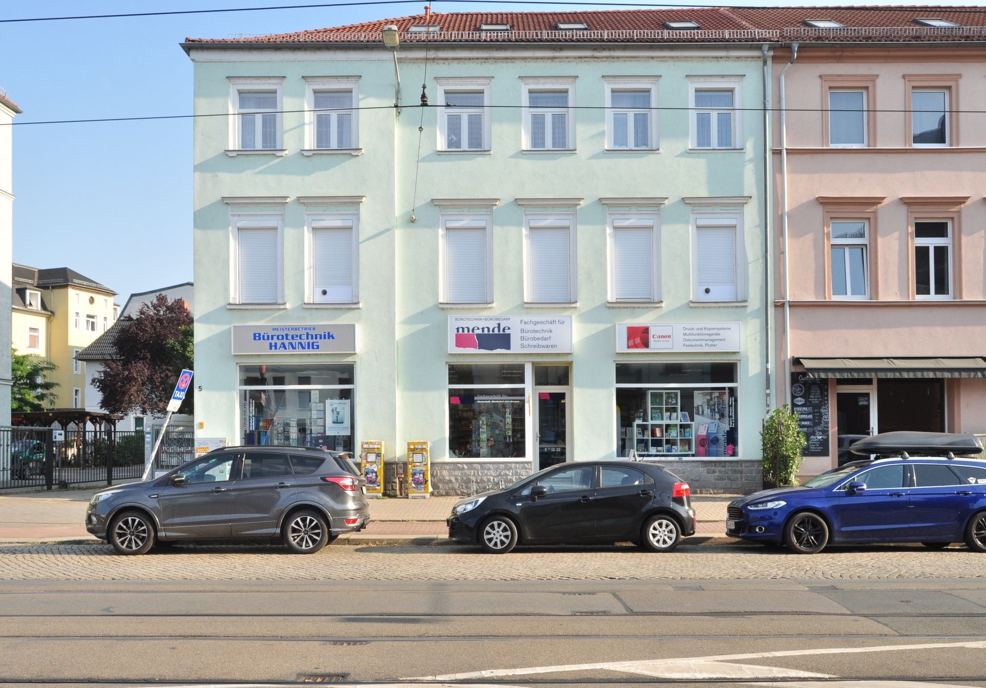Ein dreistöckiges Gebäude mit Geschäften und geparkten Autos an einer Stadtstraße.
