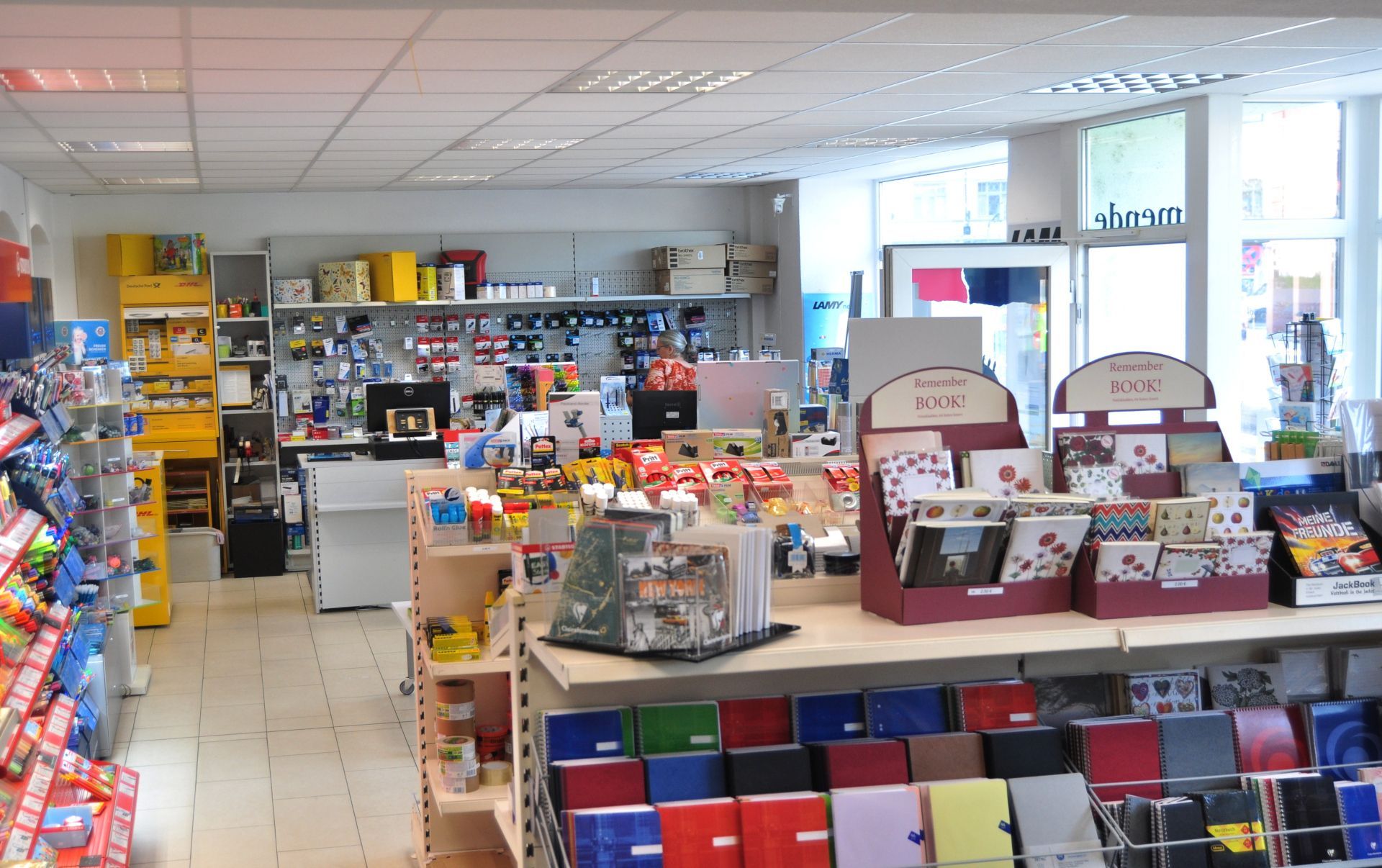 In einem Schreibwarenladen: Regale voller Karten, Geschenke und Bürobedarf. Weiße Wände, helles Licht.