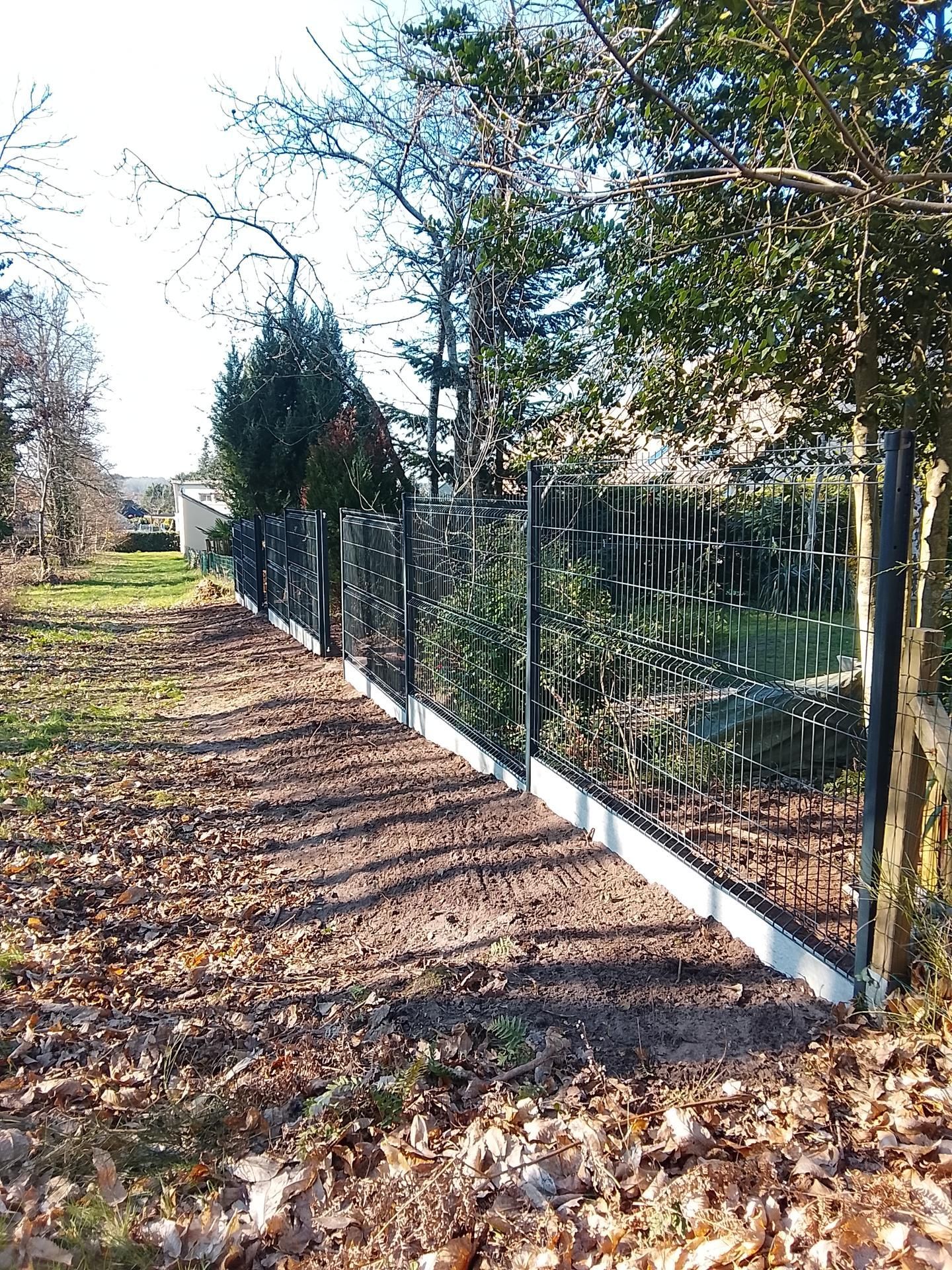 Une clôture en grillage métallique sur socle en béton.