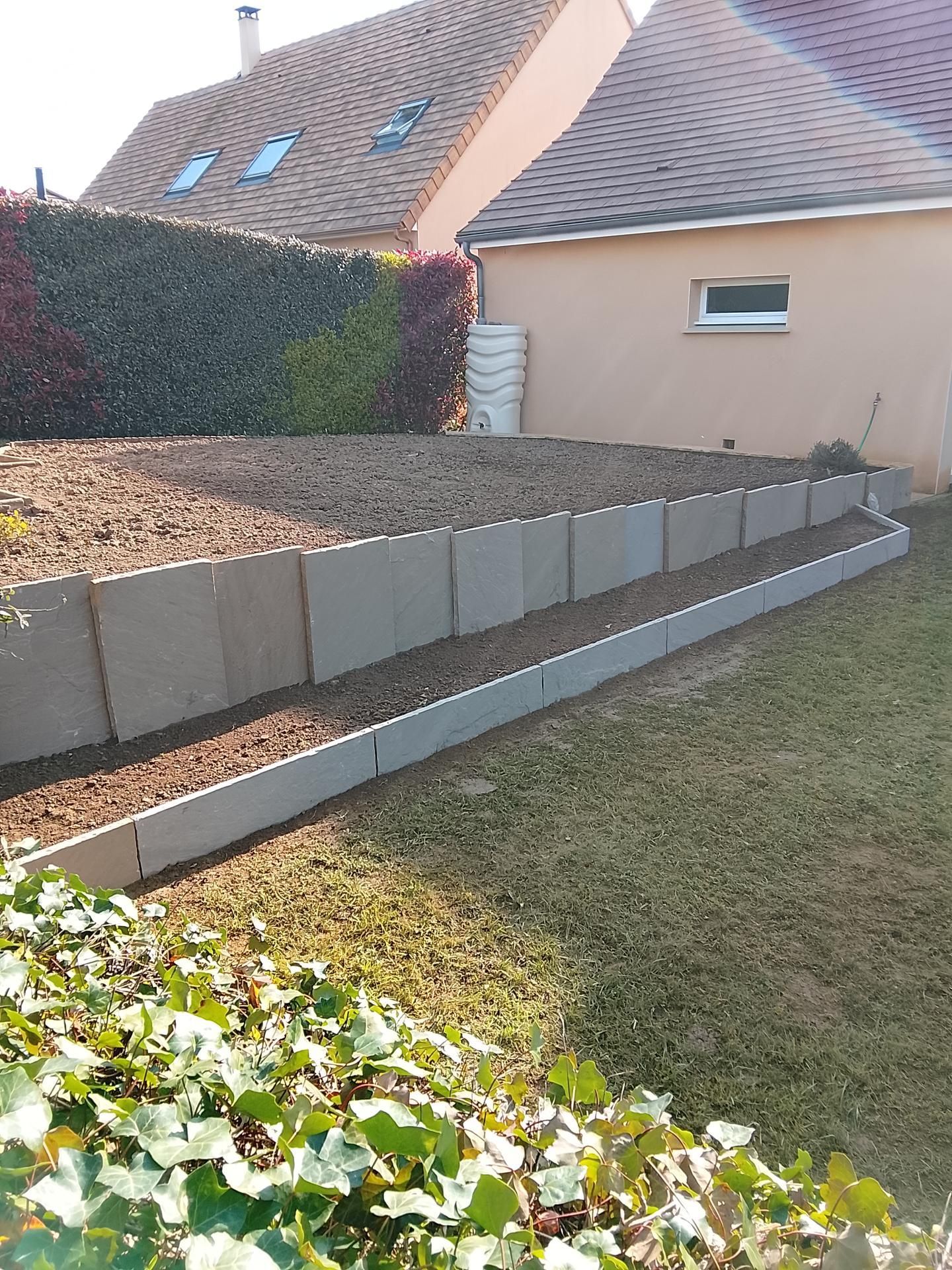 Un parterre de jardin en terrasses avec des murs de soutènement en béton gris.