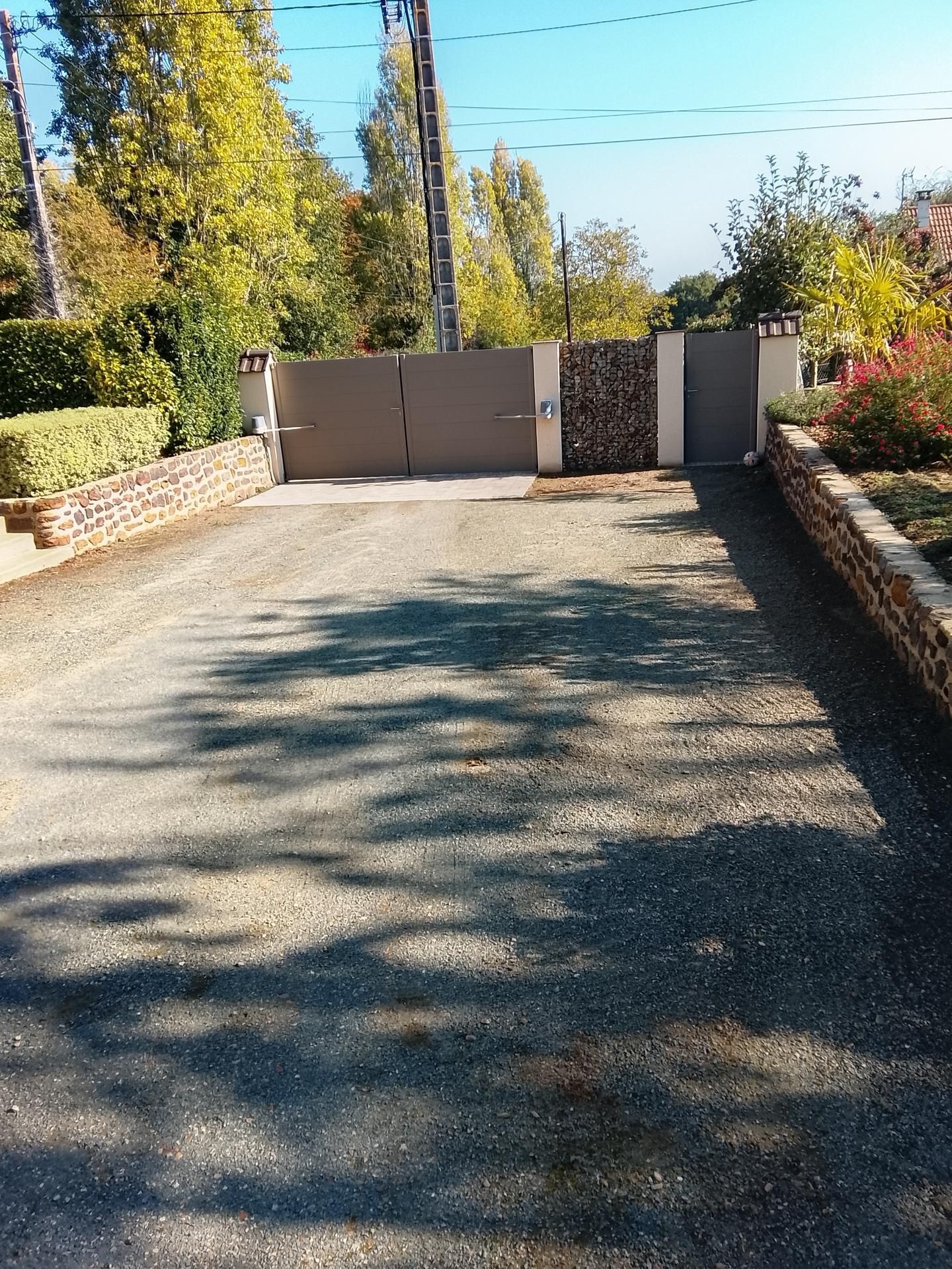 Une allée de gravier mène à un portail gris fermé.