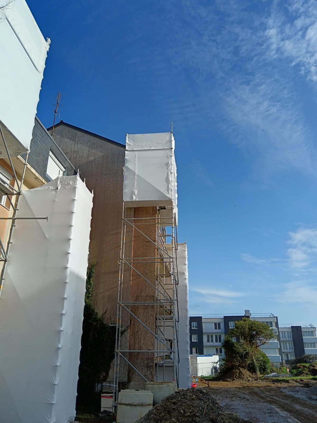 Bâtiment en construction avec échafaudages bâchés.