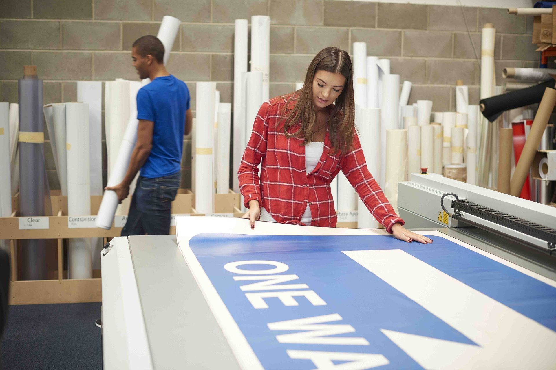 Mujer con camisa roja cortando un cartel azul y blanco, hombre con camisa azul sosteniendo