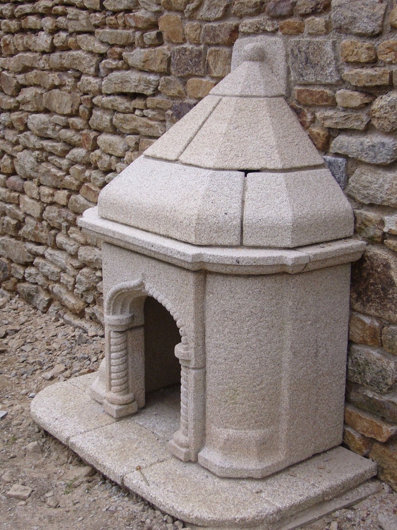 Construction d'une niche en pierre avec un toit en forme pointu. Niche située contre un mur.