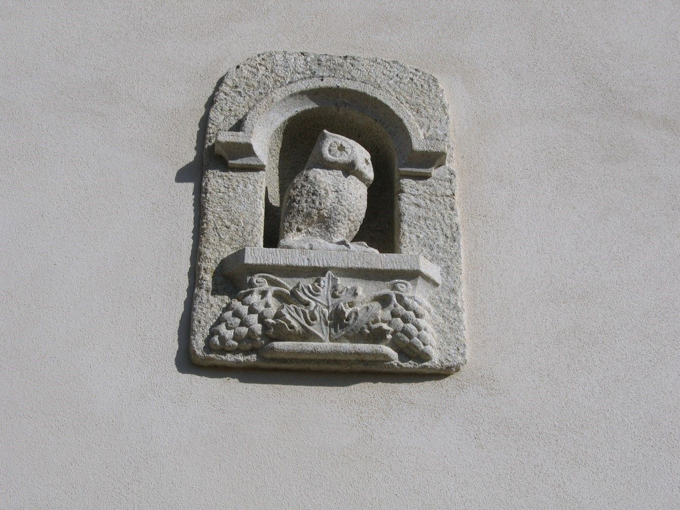 Sculpture murale d'une chouette avec des grappes de raisins en dessous.