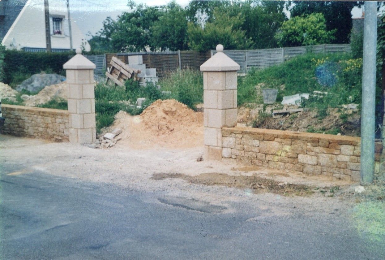 Entrée d'une propriété avec un mur en pierre comme clôture et 2 piliers en pierre pour délimiter l'entrée.