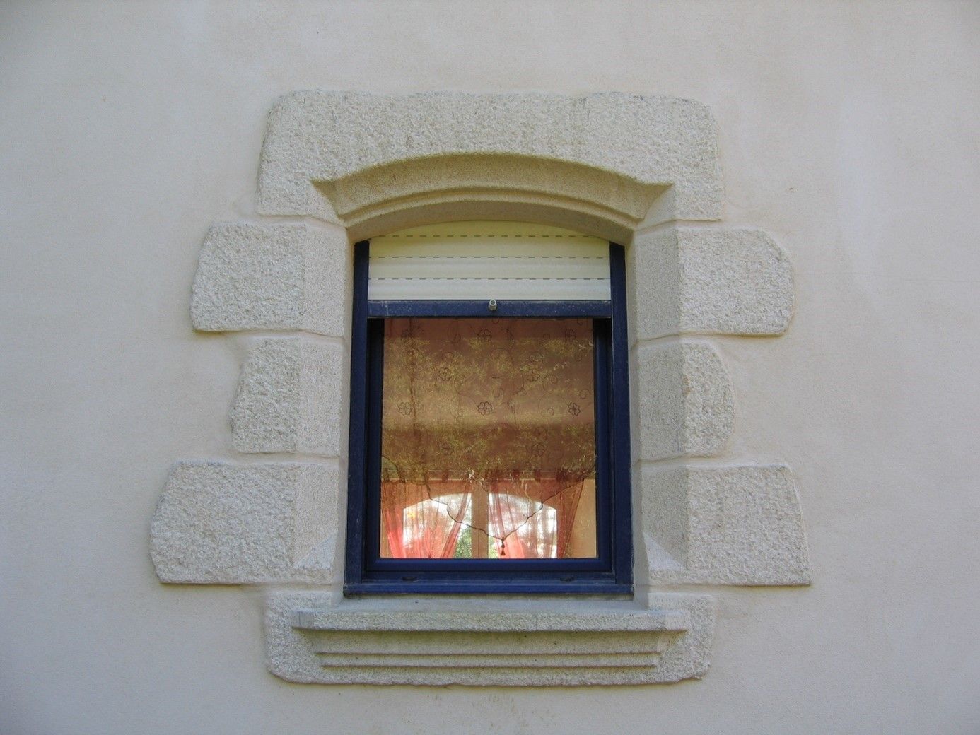 Encadrement de fenêtre en pierre. Fenêtre bleue avec des stores blancs.