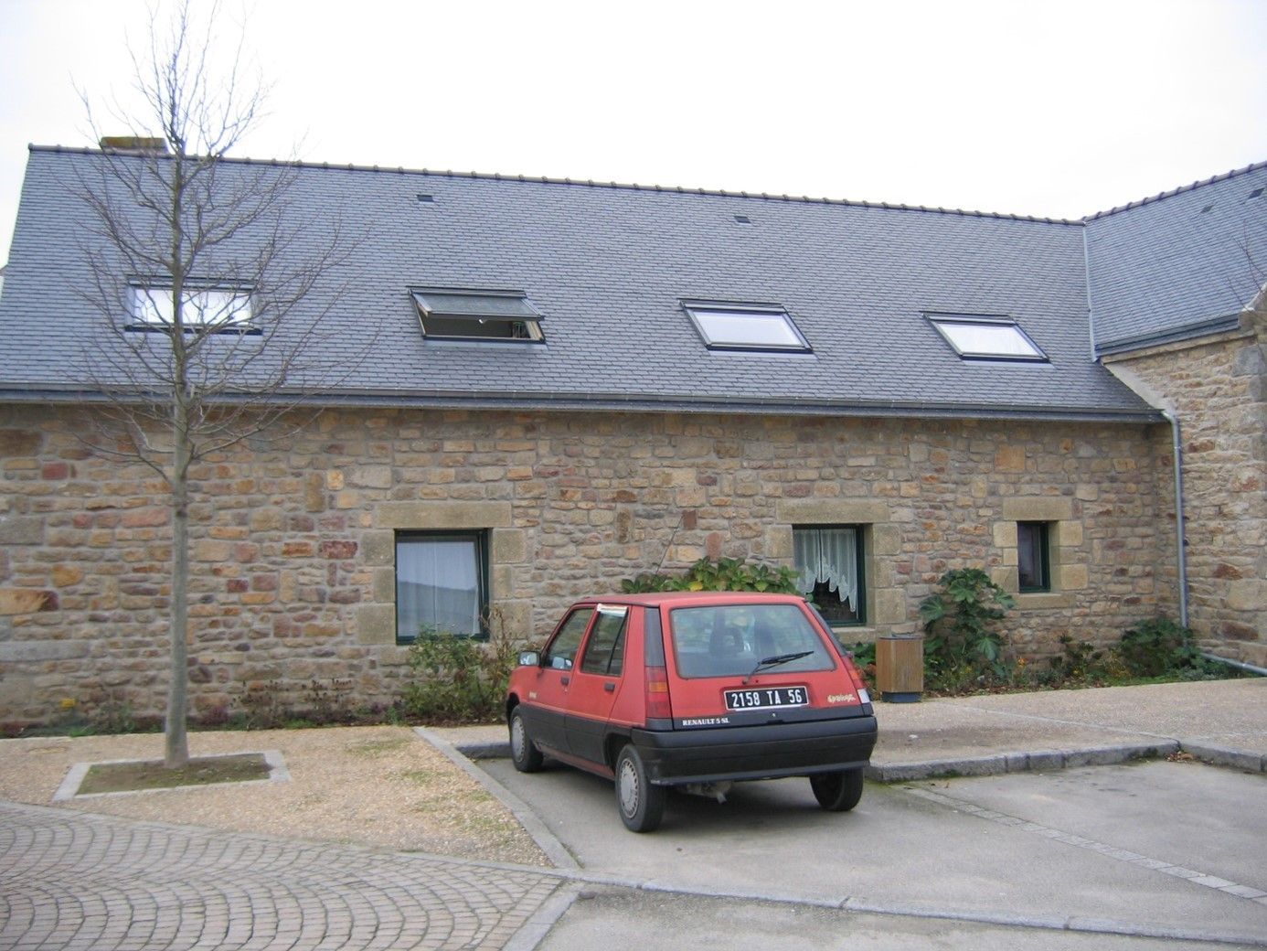 Ferme en pierre rénovée avec des fenêtres aux contours noirs et des encadrements de fenêtres en pierre.