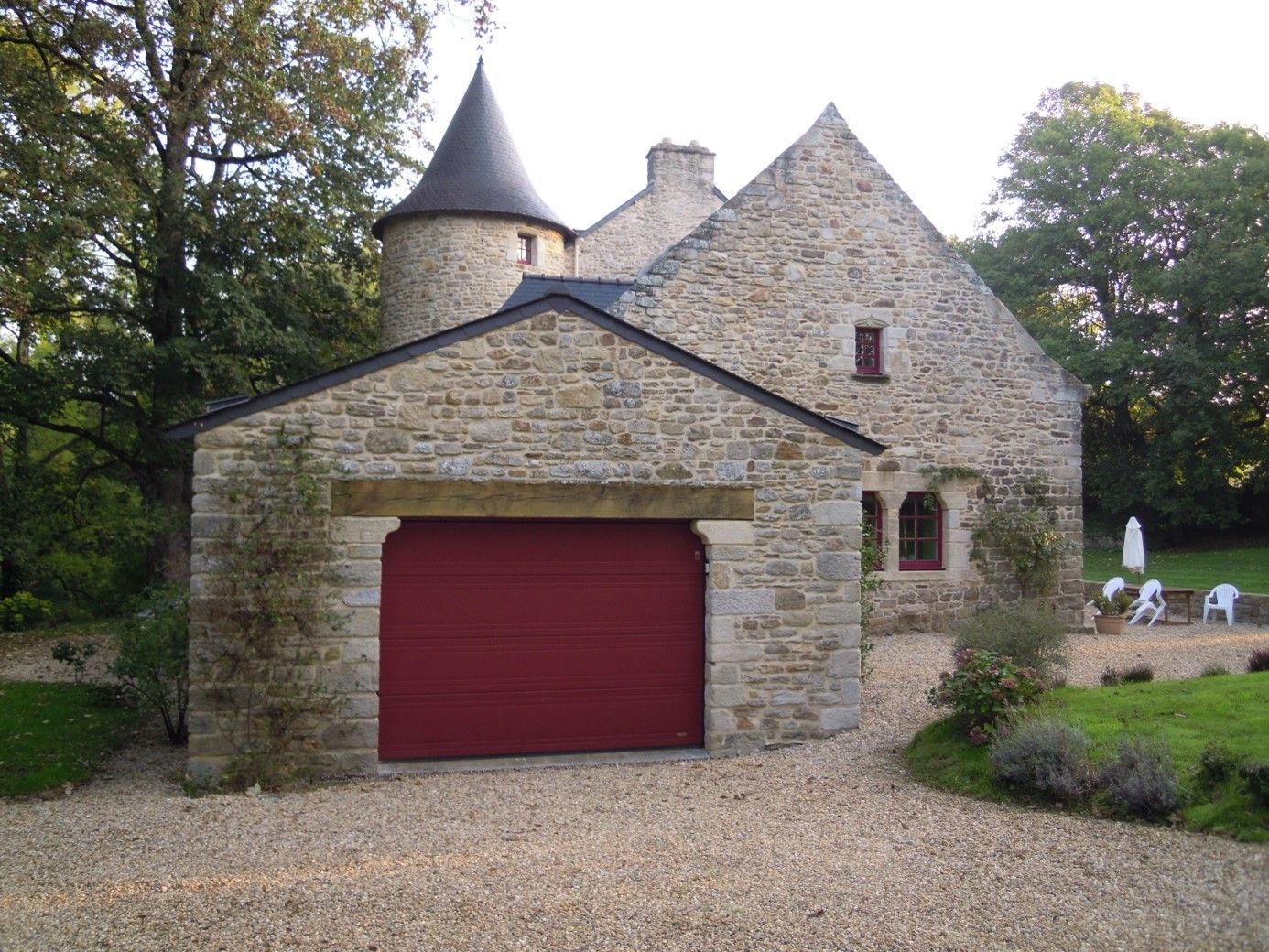Résidence en pierre avec une tour. Garage en pierre avec un portail rouge.