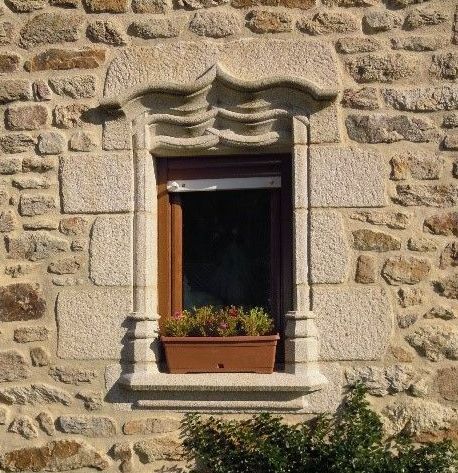 Encadrement en pierre d'une fenêtre en bois. Haut et bas sculpté pour donner des formes arrondies.