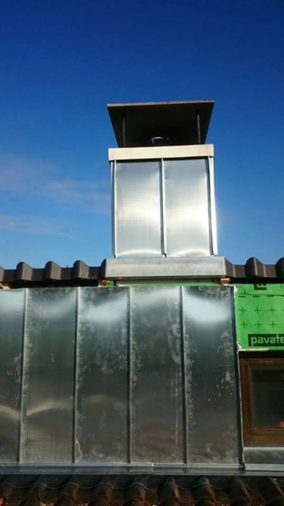 Ein Metallschornstein auf einem Gebäude mit einem blauen Himmel im Hintergrund. Foto von Ulrich Gerber Rund Ums Dach