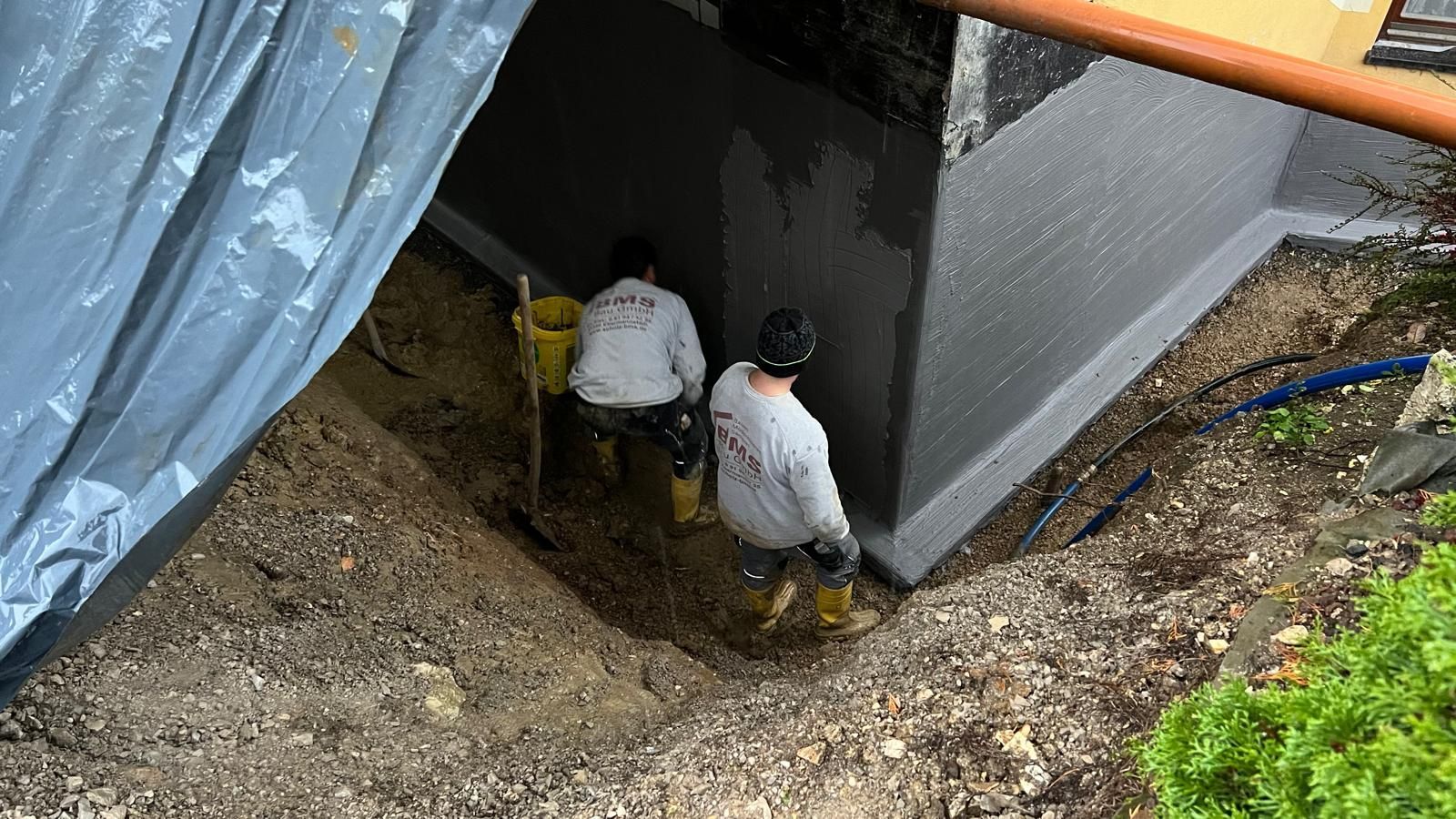 Zwei Männer graben neben einem Gebäude ein Loch in den Boden.