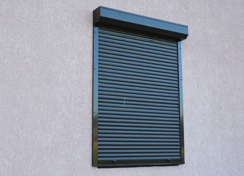 Persiana enrollable de color gris oscuro sobre una pared de estuco.