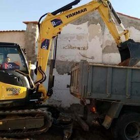 Excavadora amarilla cargando escombros en un camión en una obra de demolición.