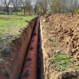 Una gran tubería roja colocada en una zanja estrecha junto a un terraplén excavado en un campo cubierto de hierba.