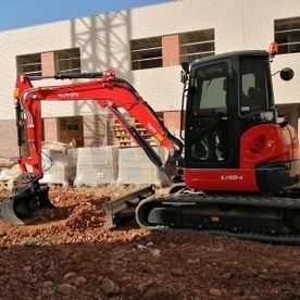 Excavadora roja en una obra en construcción junto a un edificio, removiendo escombros.