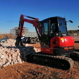Miniexcavadora roja sobre orugas cargando rocas en una obra de construcción.