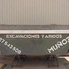 Camión volquete gris con la inscripción “EXCAVACIONES Y ARIDOS” estacionado contra una pared ondulada.