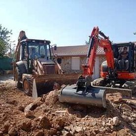 Dos excavadoras retirando escombros en una obra en construcción cerca de una casa.