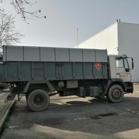 Camión volquete gris estacionado junto a un edificio en un terreno pavimentado.