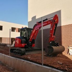 Excavadora roja estacionada junto a un edificio en una obra de construcción de tierra.