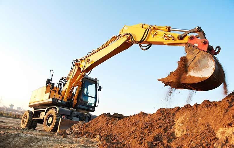 Excavadora amarilla cavando un montículo de tierra en una obra de construcción bajo un cielo despejado.