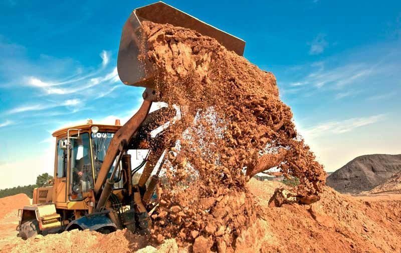 Excavadora descargando tierra en una obra bajo un cielo azul.