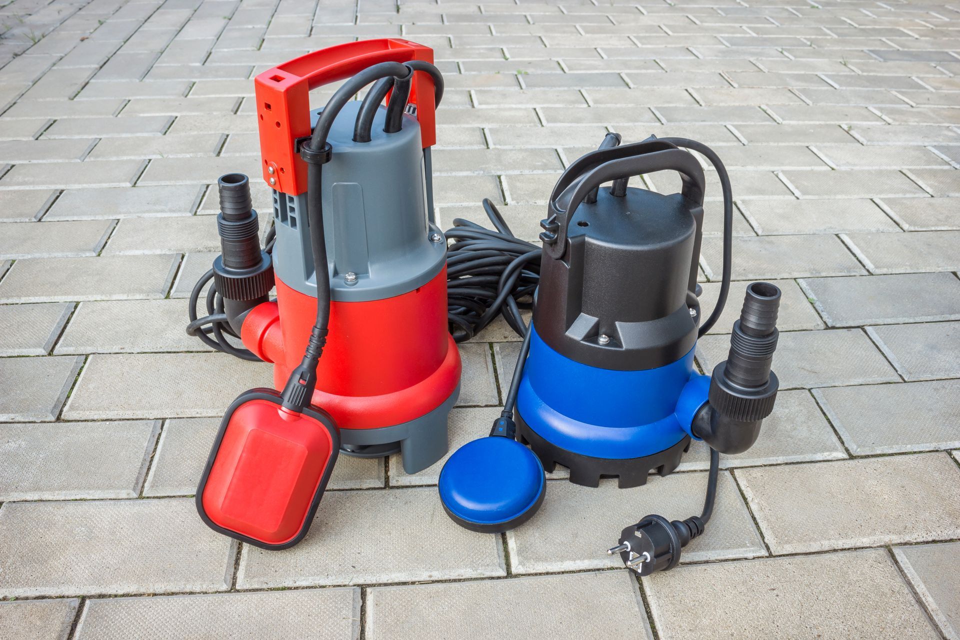 Deux petites pompes submersibles, une rouge et une bleue, posées sur une route pavée.