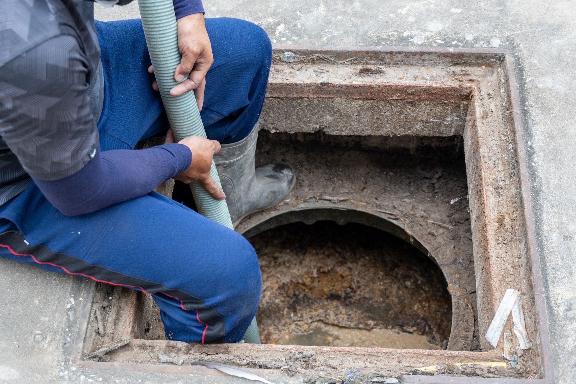 Un ouvrier utilise un tuyau pour vidanger un regard d'égout ouvert dans un sol en béton.