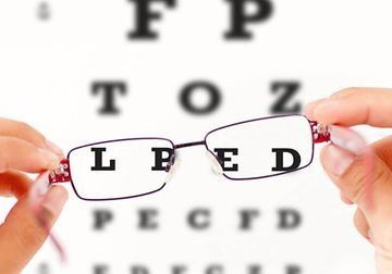 Una persona sostiene un par de gafas delante de una tabla optométrica.