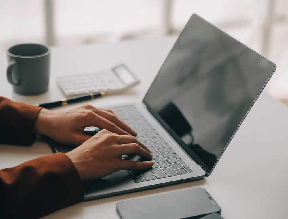 Una persona está escribiendo en una computadora portátil en un escritorio.