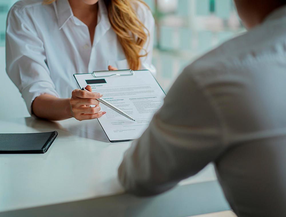 Una mujer sostiene un portapapeles y señala a un hombre durante una entrevista de trabajo.