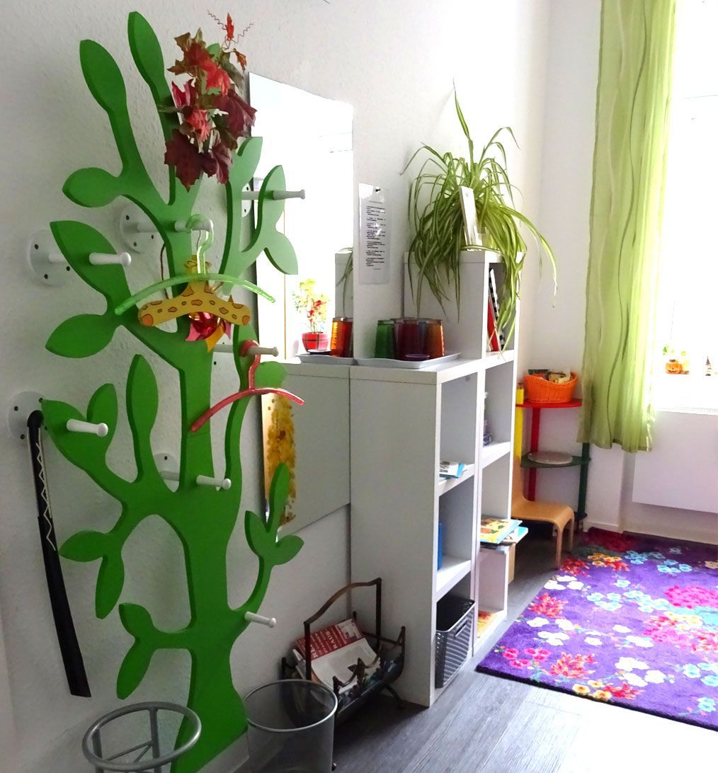 Grüne Garderobe mit Mänteln, neben einem weißen Regal und einem lila geblümten Teppich in einem Zimmer.