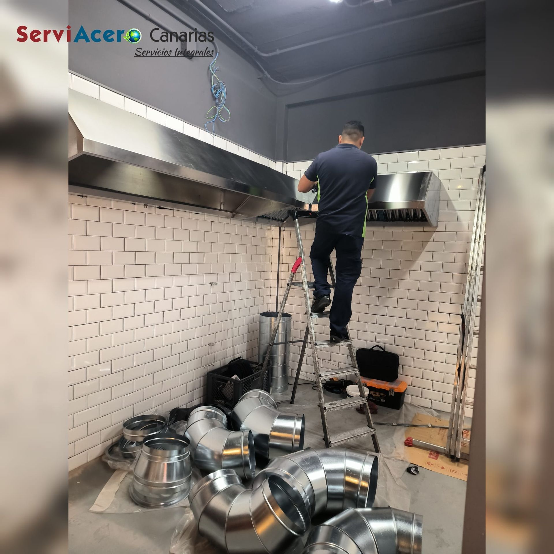 Un hombre está de pie en una escalera en una cocina rodeada de tuberías.