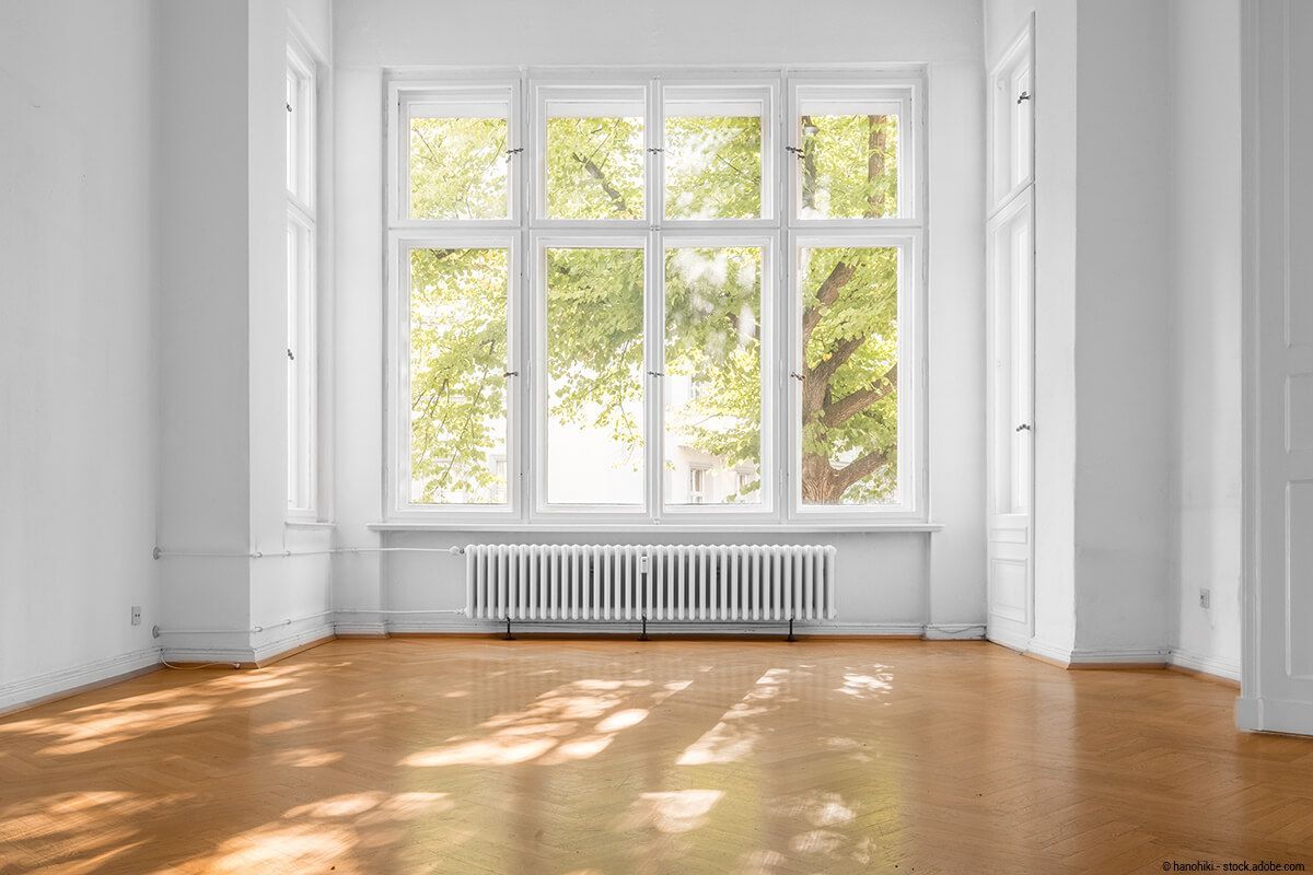 Leerer weißer Raum mit Holzboden, großen Fenstern und Sonnenlicht, das Baumschatten auf den Boden wirft.