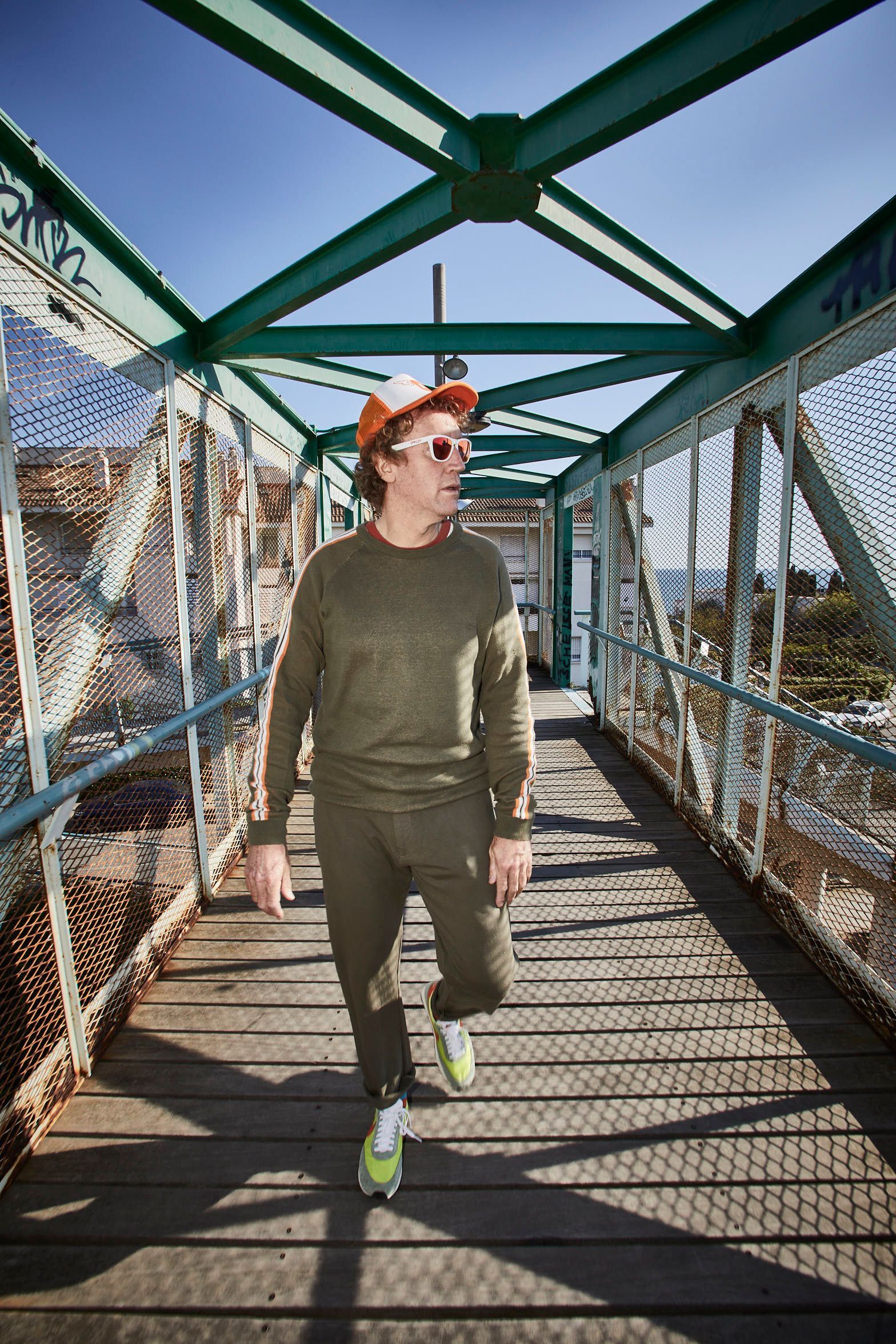 Un hombre camina por un puente con sombrero y gafas de sol.
