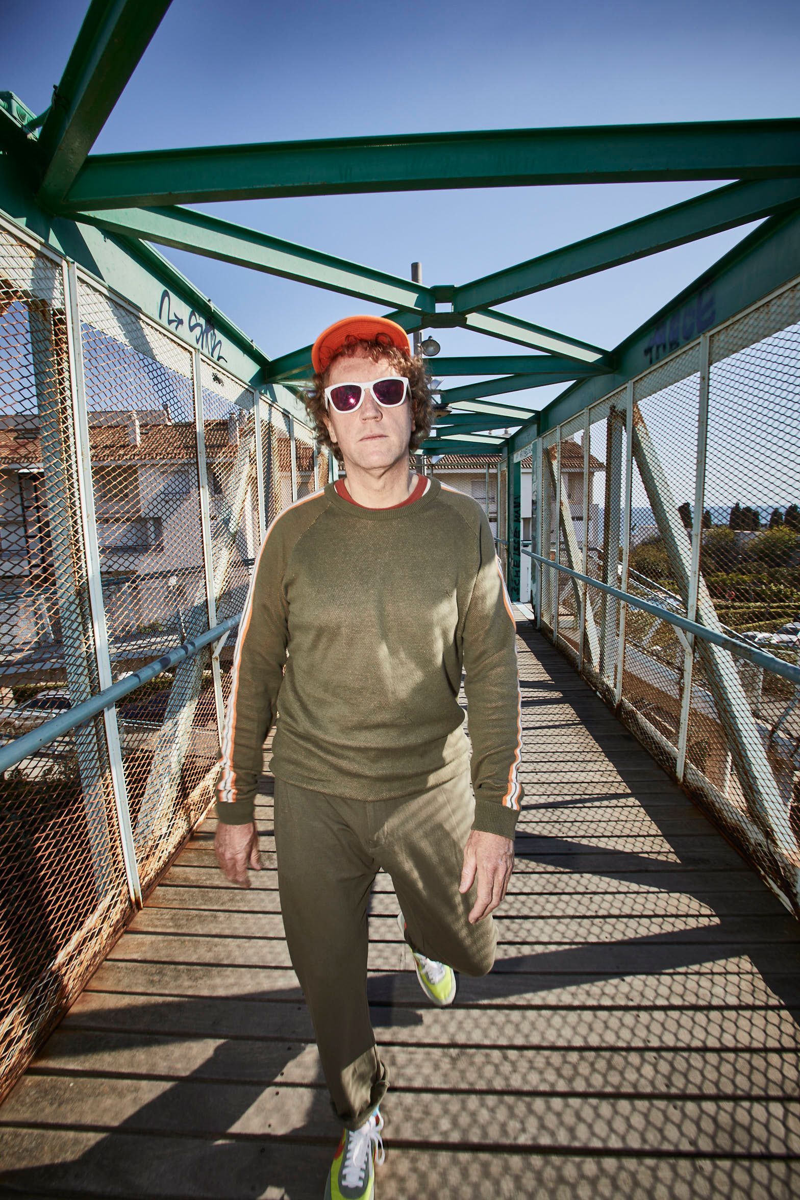 Un hombre que lleva gafas de sol y sombrero camina por un puente.