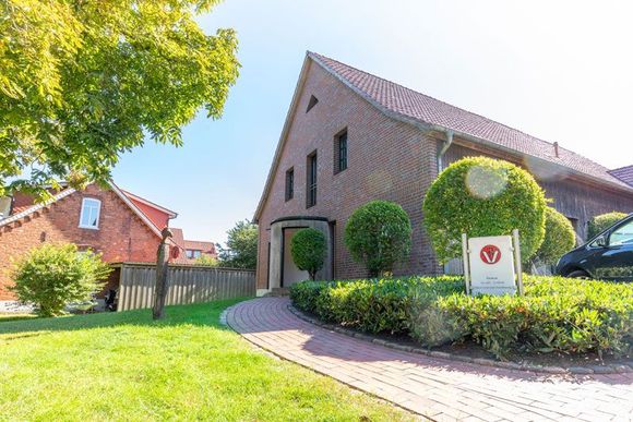 Backsteinhaus mit gepflegten Hecken und gepflasterter Auffahrt in einer sonnigen Vorstadtstraße