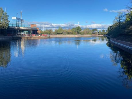 Río azul tranquilo con árboles, un puente a la izquierda y un cielo despejado reflejado en el agua.