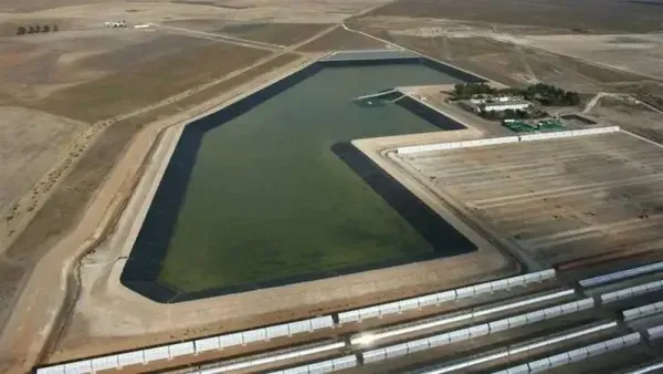 Vista aérea de un gran embalse de agua verde junto a edificios industriales en un paisaje seco y árido.
