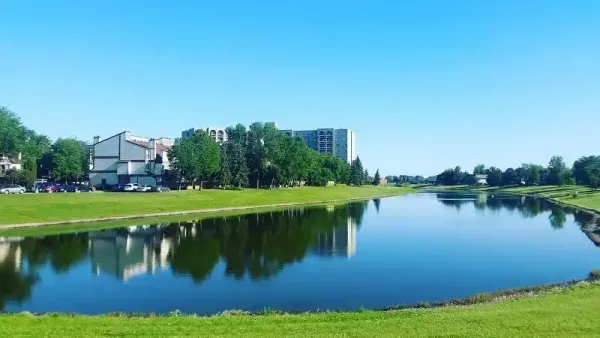 Río tranquilo que refleja el cielo azul, las orillas verdes y los edificios de apartamentos en un día soleado.
