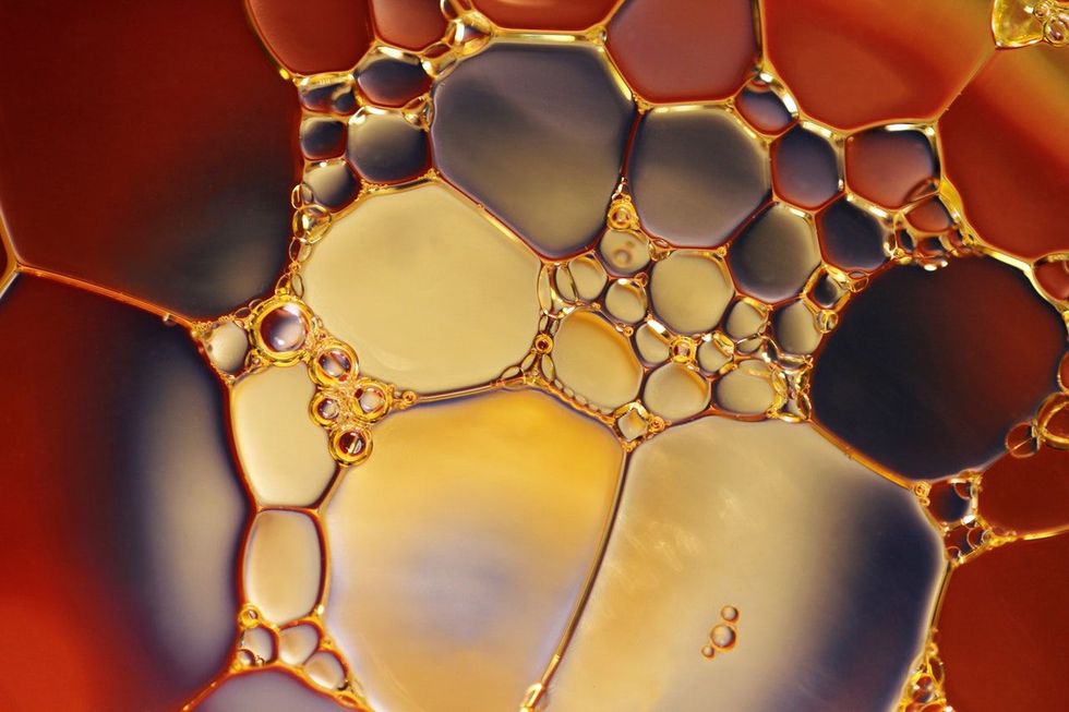 Primer plano abstracto de burbujas y gotitas de líquido ámbar y dorado con bordes rojo oscuro.