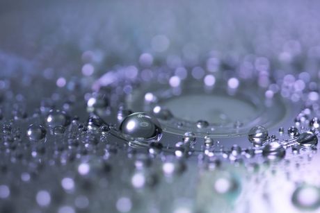 Gotas de agua moradas sobre una superficie reflectante, con una gota grande que crea ondas.
