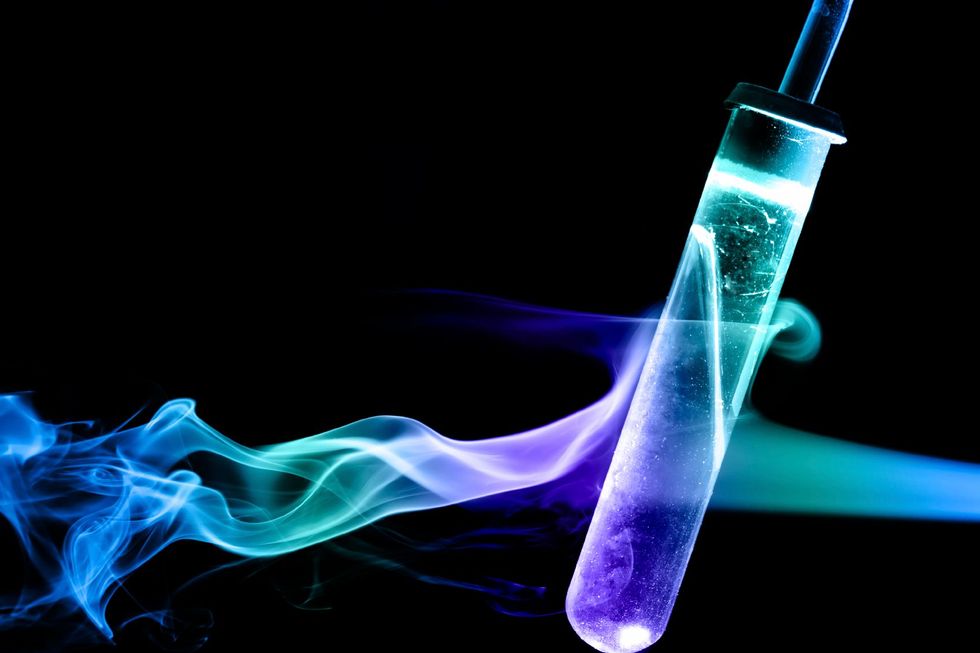 Tubo de ensayo azul-púrpura brillante con humo de neón arremolinado sobre un fondo negro.
