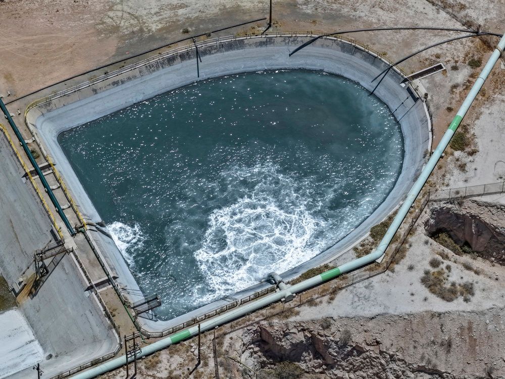 Vista aérea de una balsa industrial circular con agua oscura y turbulenta, rodeada de hormigón y tuberías.
